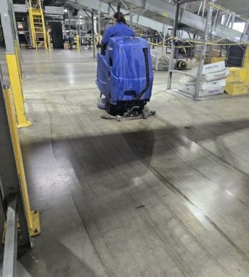 Warehouse cleaner using ride-on floor scrubber in an industrial facility